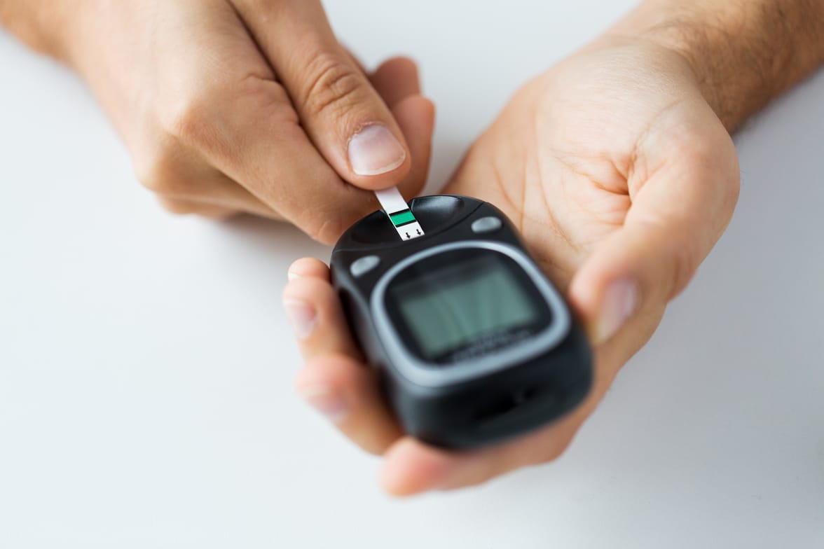 medicine, diabetes, glycemia, health care and people concept - close up of man checking blood sugar level by glucometer and test stripe at home